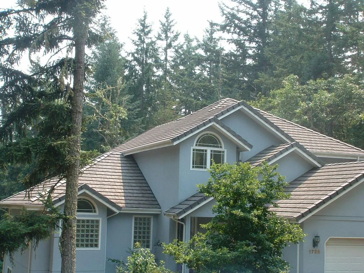 Modern grey house among tall trees with a sloped roof and large arched window.