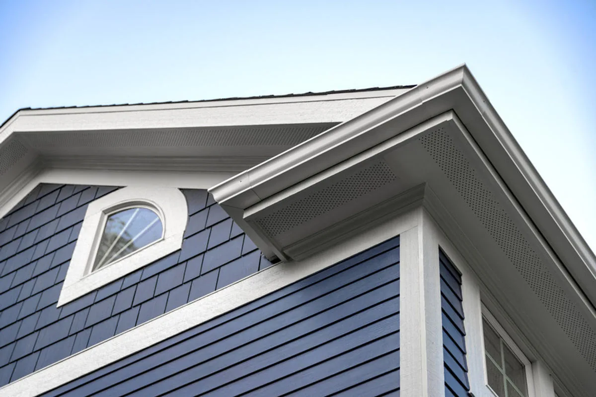 Blue house exterior with detailed trim and roofing against a clear sky.